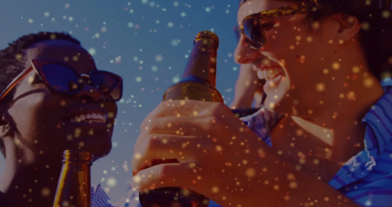 Hände stoßen braune Flaschen an, zwei Erwachsene prosten und trinken unter einem Partikel-Overlay für Marketingzwecke.