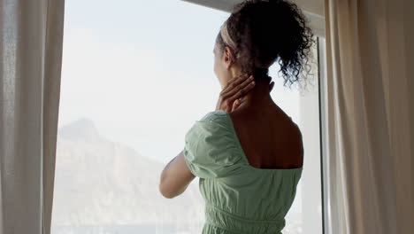 woman in green dress pointing outside window, wearing smartwatch, looking curious, at home