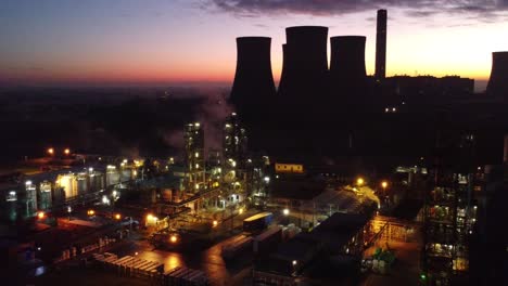 illuminated aerial night view above industrial pipeline chemical factory site slow zoom out reveal shot