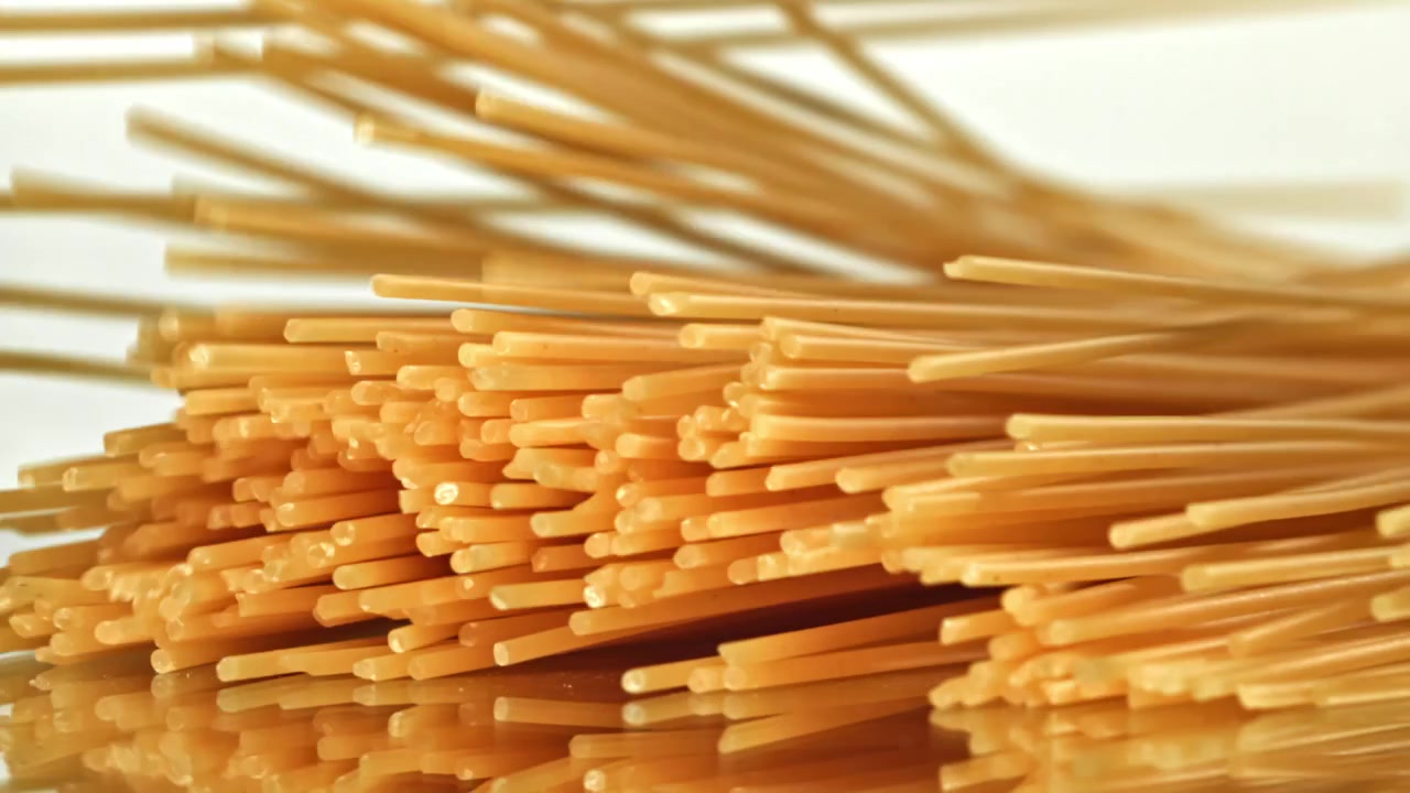 Spaghetti secchi che cadono al rallentatore su sfondo bianco