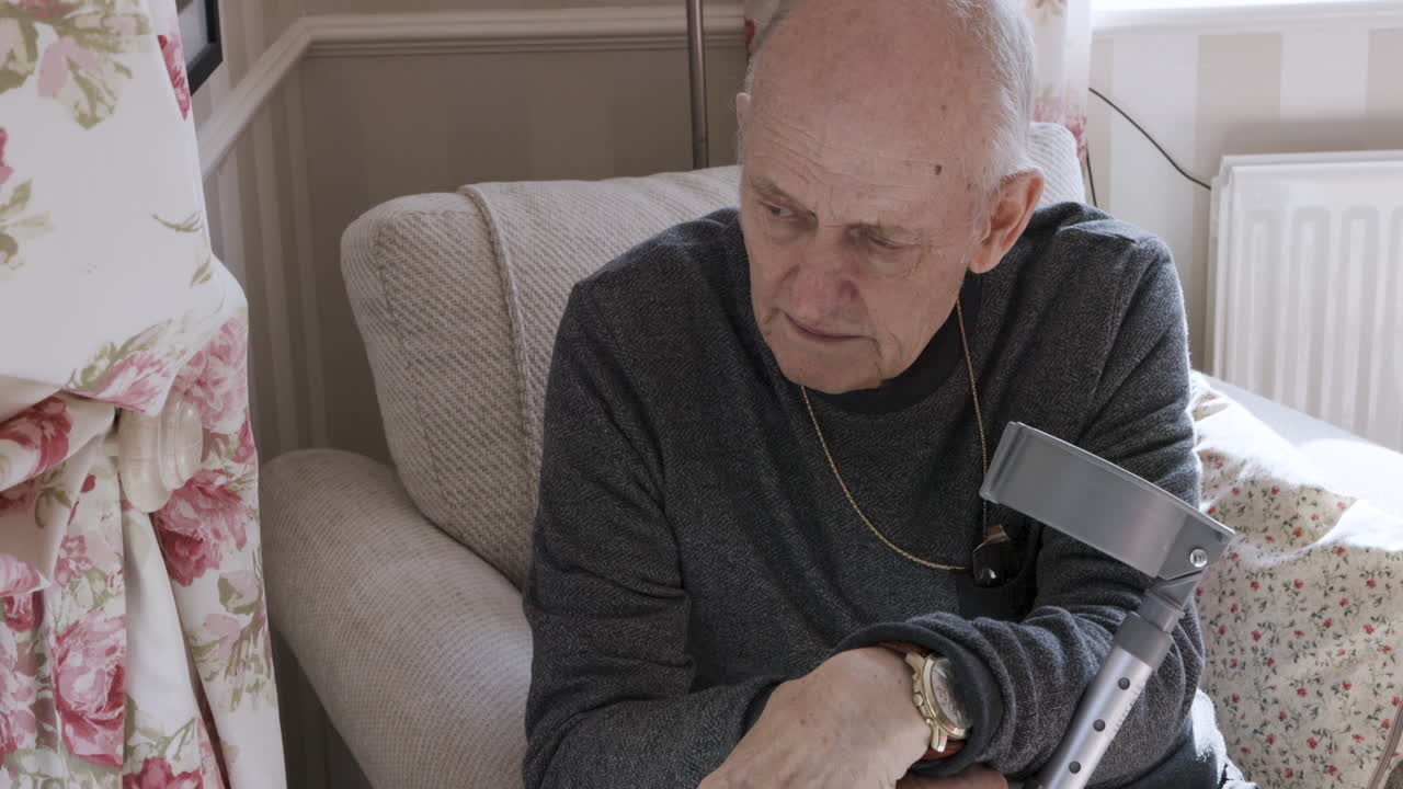 Elderly man sitting in armchair with crutch