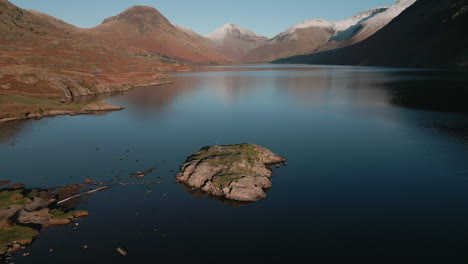 flying down to hiker on island in dark lake with snowy mountain range reveal at wasdale lake district uk