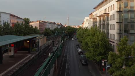 Forwards-tracking-of-city-train-driving-on-elevated-railway-in-Schoenhauser-Allee-street.-Ascending-footage-reveals-cityscape-lit-by-bright-morning-sunshine.-Berlin,-Germany