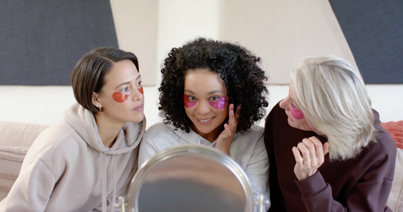 Diverse women friends with senior on couch checking mirror and adjusting eye patches during demo