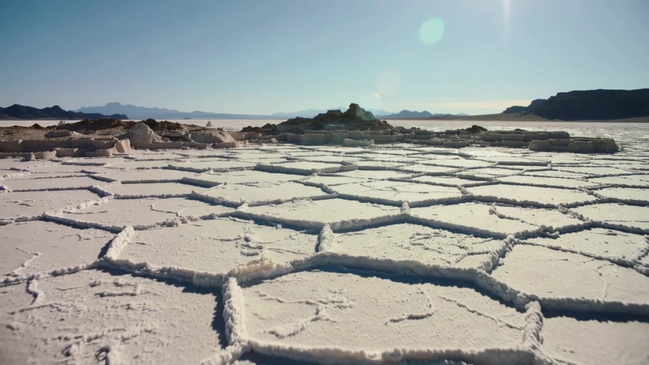 Shot starting, pulling back camera over salt pan, revealing hex salt plates, sun flare toward ridge