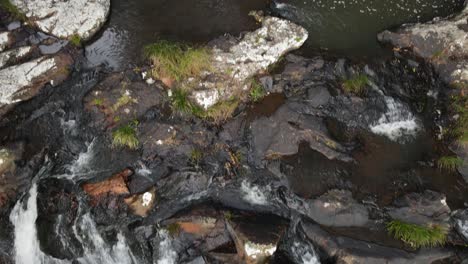 Slow-reveal-of-a-rainforest-creek-flowing-down-towards-a-waterfall-cascading-into-a-deep-tropical-rock-pool-below