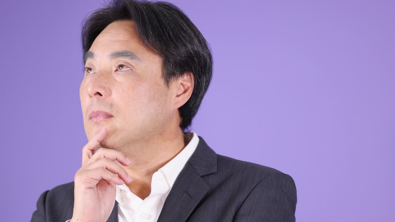 Businessman in suit ponders thoughtfully, hand on chin, under soft studio lighting, purple background