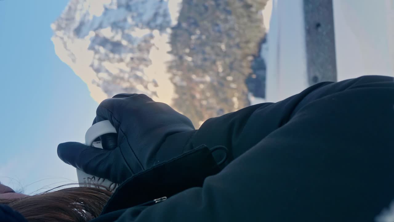 여성이 뜨거운 차나 커피를 마시고 축제 컵에서 뒤에 눈이 내린 산을 바라보고 있습니다.