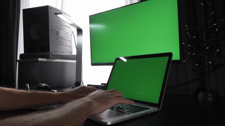 Chroma key green screen. Man is working on laptop computer with green screens, typing on keyboard at workplace in modern office. Male is using pc on desk, working from home. Technology concept