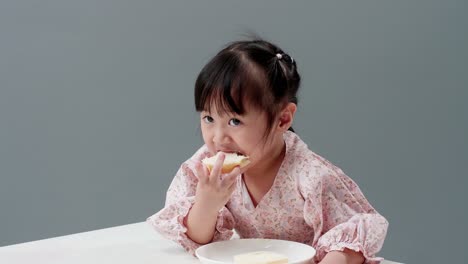 asiatic child eating piece of sweet in the studio with a gray background