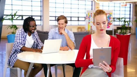 Frau-Mit-Digitalem-Tablet-Und-Kollegen,-Die-Im-Hintergrund-Am-Laptop-Arbeiten