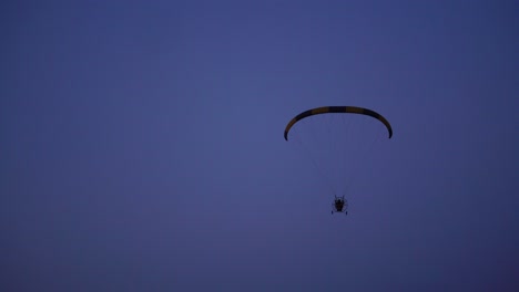 The-pilot-on-a-paraglider-flies-from-the-camera-gradually-moving-away-into-the-distance-against-the-blue-sky