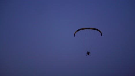 the pilot on a paraglider flies from the camera gradually moving away into the distance against the blue sky