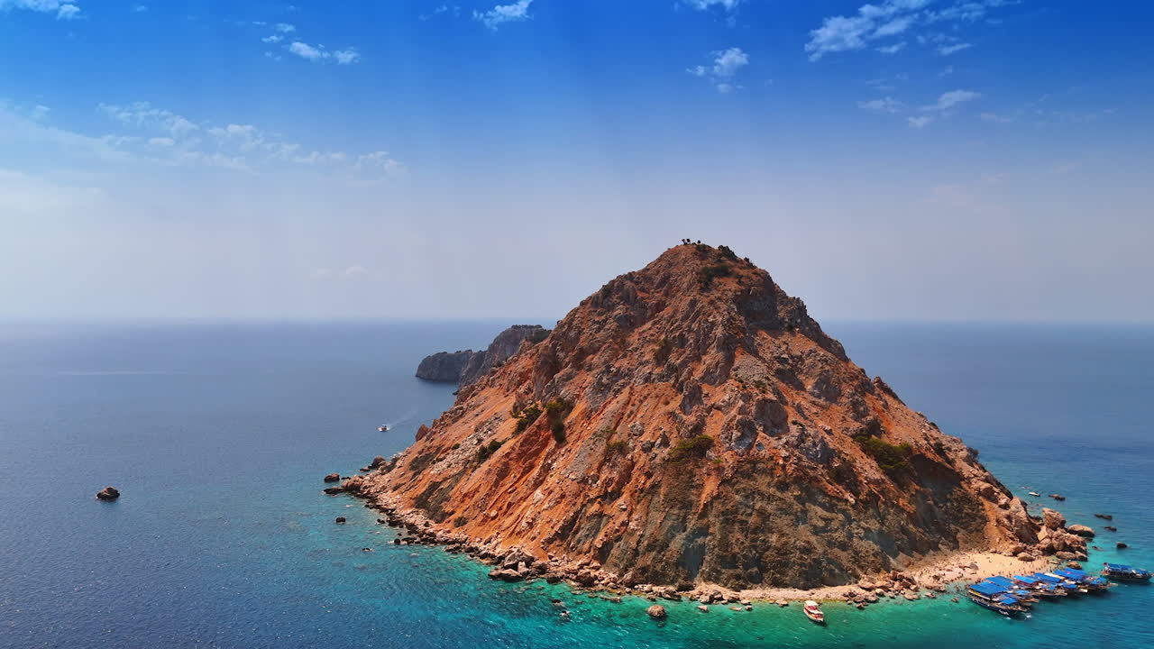 Island rising from the clear blue sea. A rocky island stands prominently against the azure ocean, surrounded by calm waters and a bright sky