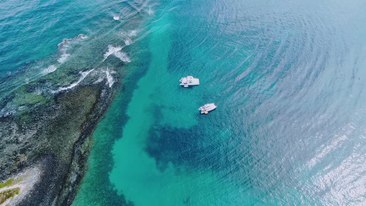 Arcipelago di Abrolhos vicino a Caravelas, Bahia, Brasile, con laguna di barriera corallina poco profonda e chiazze di barriera più scure in acque limpide dell'Atlantico meridionale, con barche ancorate all'interno di un parco nazionale marino, volo lento dall'alto