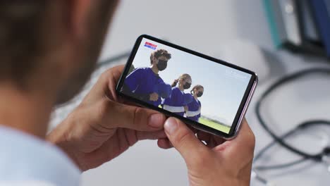 Zusammensetzung-Eines-Männlichen-Arztes,-Der-Während-Covid-19-Ein-Baseballspiel-Auf-Dem-Smartphone-Beobachtet