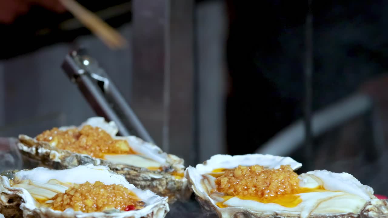 A detailed view of oysters being grilled, with visible steam and tongs in action.