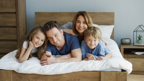 padres alegres y sus hijos acostados en la cama y sonriendo a la cámara por la mañana