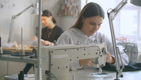 Frau-Näherin-Arbeitet-An-Einer-Nähmaschine-In-Der-Werkstatt-Zum-Nähen-Von-Kleidung.-Zusammenarbeit-In-Einer-Nähwerkstatt