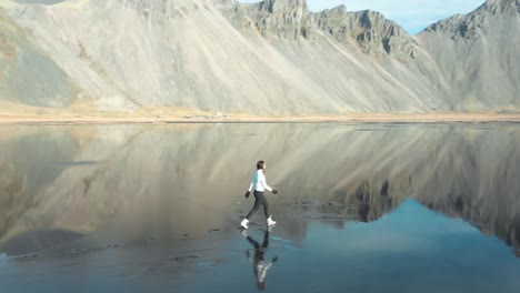 Mujer-Caminando-Sobre-El-Agua-Reflexión-Playa-Islandia-Drone-Antena