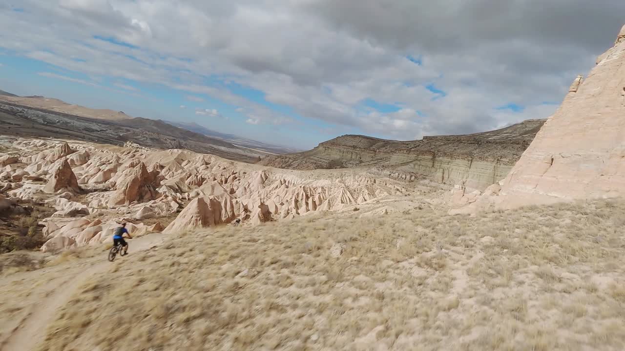 Volando verso i paesaggi montuosi aridi e rocciosi con due ciclisti attivi che scendono pendii ripidi in Cappadocia, Turchia