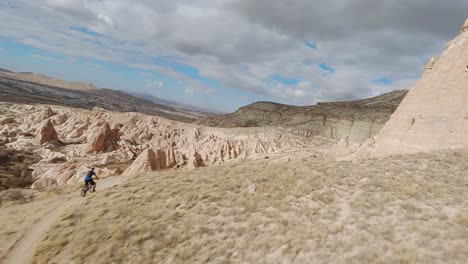 flying towards the arid rocky mountain landscapes with two active bikers riding down steep slopes in cappadocia, turkey