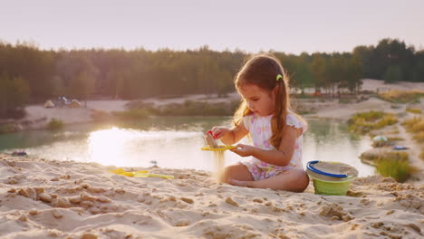 a girl of three years playing in the sand on a background of lake and recreational
