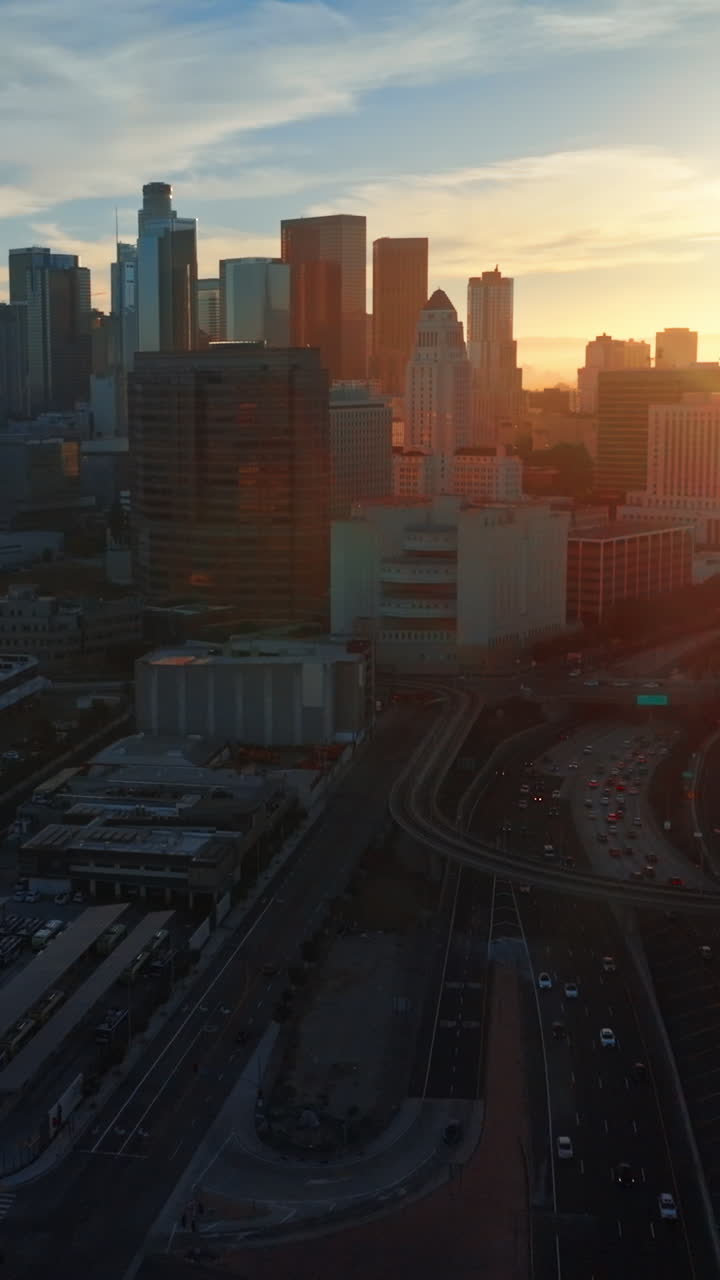 Excellent scenery of Los Angeles downtown in the evening. Numerous cars moving quickly by the highways. Bright sun at backdrop. Vertical video