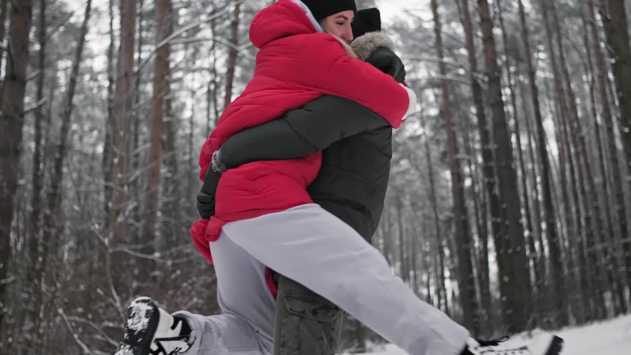 행복한 젊은 부부는 겨울의 숲에서 데이트를 하고 재미를 느끼고 있습니다. 남자가 여자를 안고 있습니다.