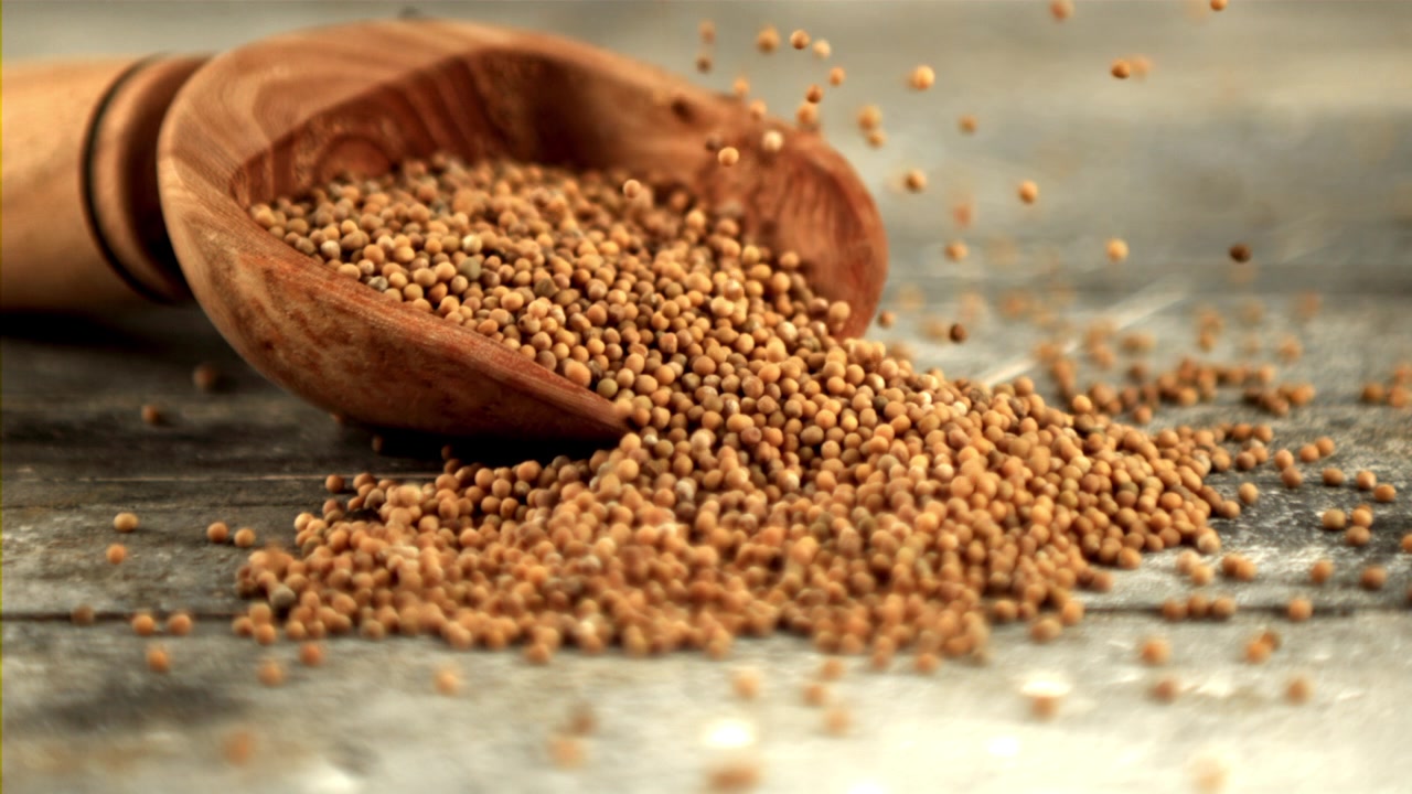 Mustard Seeds Pouring from a Wooden Scoop in Slow Motion