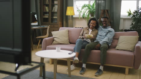 smiling afro couple watching comedy on tv