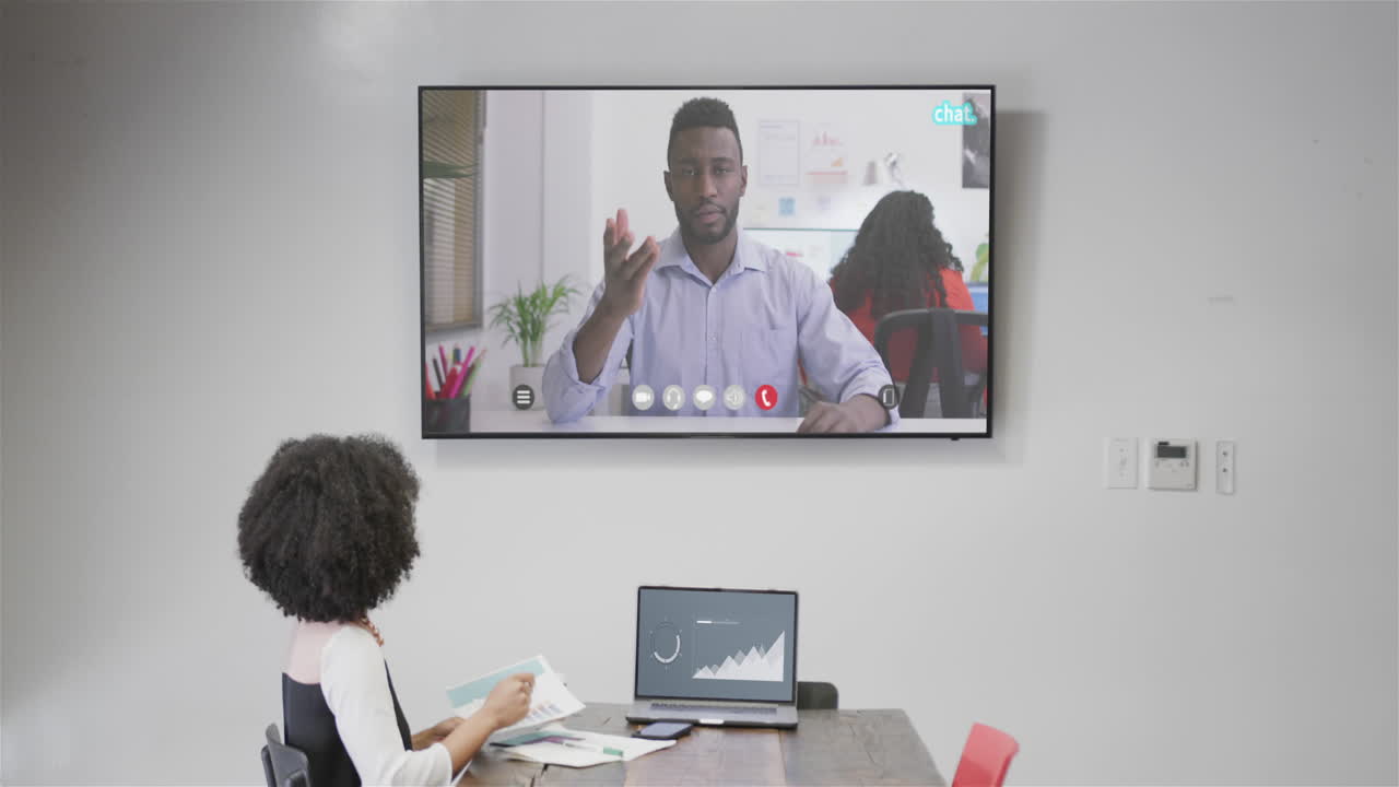 mujer de negocios afroamericana en videoconferencia con su colega afroamericano en la pantalla de televisión