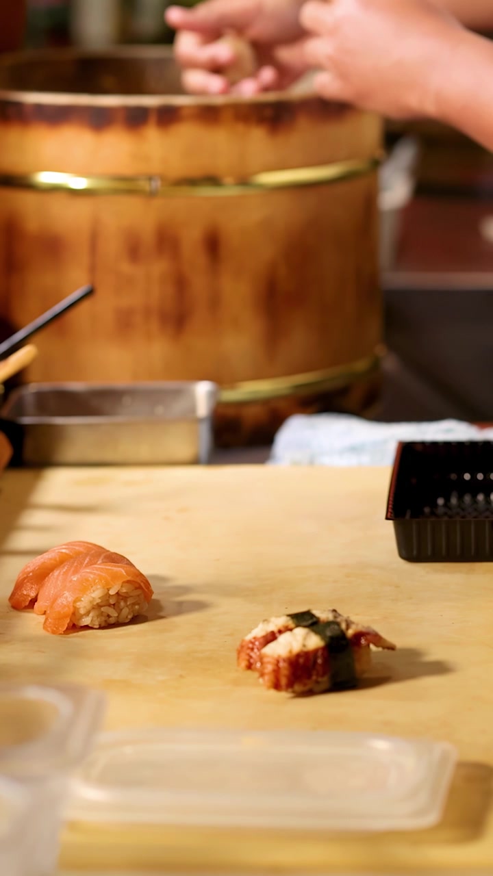 Um chef habilidoso prepara nigiri de salmão e enguia numa tábua de madeira em um restaurante.