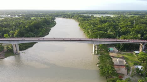 tracking aerial shot along concrete brigde connecting two forested riverbanks, bangladesh