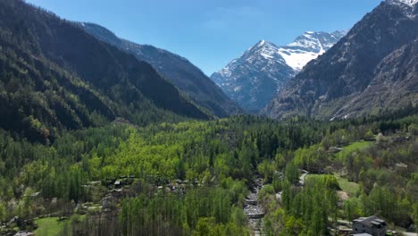 aerial dolly forward shot of a village nestled in the mountains on a clear sunny day with a snow capped mountain in looming in the background