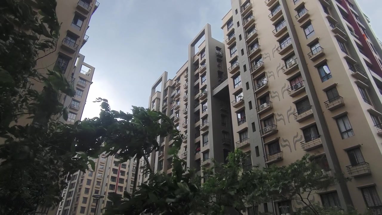 Vista en ángulo bajo de clima tormentoso en complejos de apartamentos residenciales de gran altura en India, con arquitectura moderna y exuberantes árboles verdes en primer plano. Viento soplando