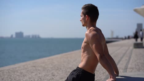 muscular shirtless man in shorts exercising at riverside