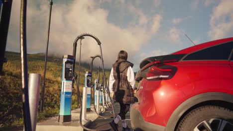 a woman charging a red electric vehicle