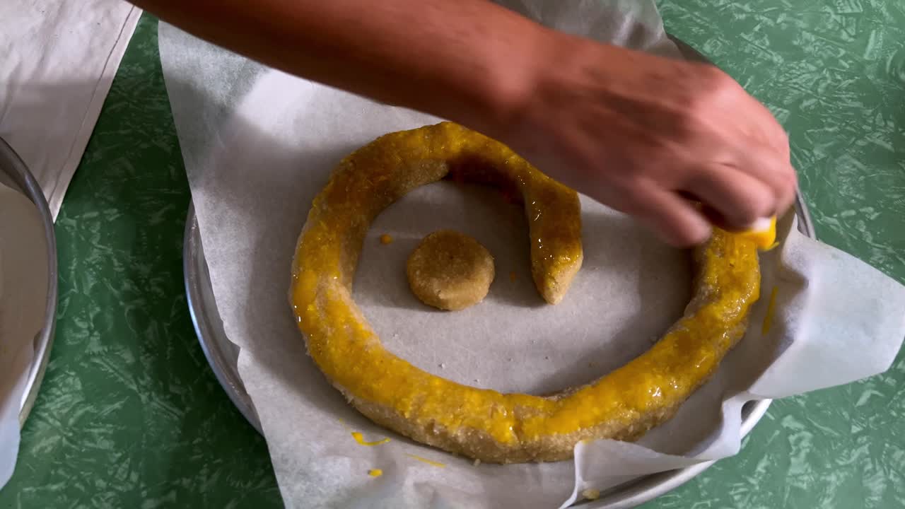 Close up of woman's hands brushing egg wash onto a traditional Italian Christmas cake, the Torciglione, before baking. For cooking or holiday content