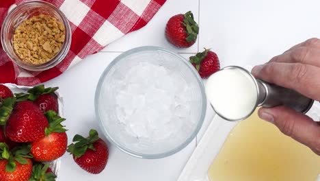 Making a Strawberry Shortcake Martini and adding in the half and half with the other ingredients. Strawberries on a red and white gingham napkin. Close up of making a cocktail for happy hour.