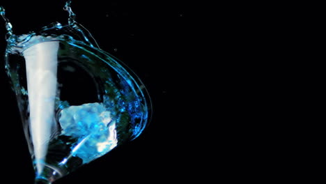 hielo cayendo en un vaso de cóctel de líquido azul