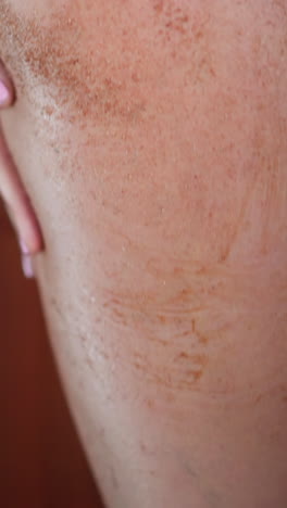 young slim woman puts anti-cellulite coffee scrub on soft skin of buttocks and thigh in shower at home against blurred wall slow motion closeup