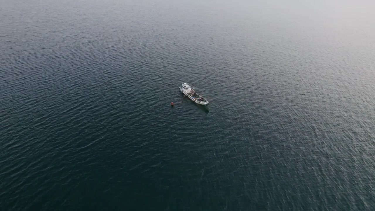 Un drone si muove intorno a una barca da pesca giapponese nel lago Biwako, con isole sullo sfondo, una destinazione di viaggio asiatica sotto uno skyline nebbioso