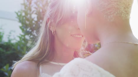 feliz pareja de mujeres diversas sosteniendo un ramo de flores y abrazándose en el jardín