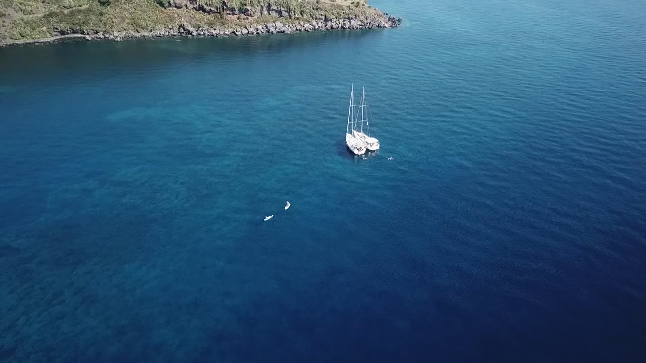 Aerial view of the boat on anchor and people on SUP in Italy, Sicily, Volcano island