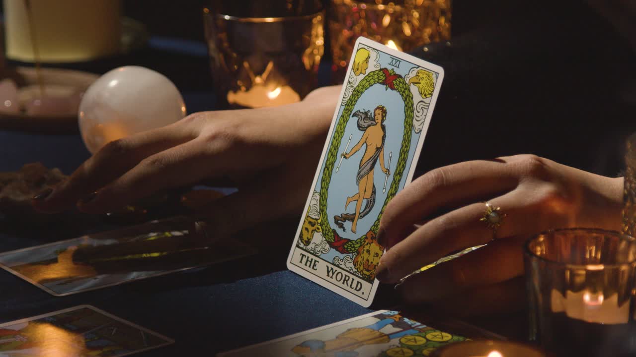 primer plano de una mujer dando lectura de cartas del tarot en una mesa a la luz de las velas sosteniendo la carta del mundo 1