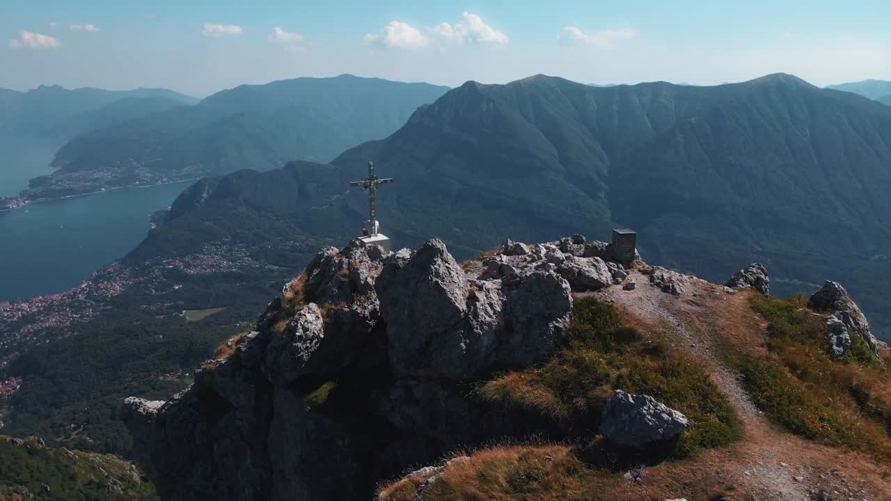 video di un drone in rapido movimento di un uomo seduto accanto alla croce in cima a monte grona vicino al lago como in italia