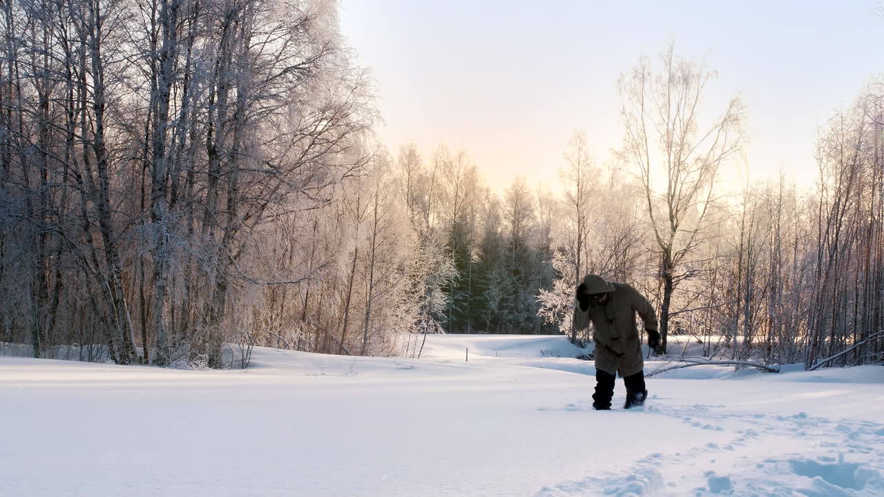 Statisk billede af en mand i en tyk frakke, der går gennem dyb sne i en frossen park