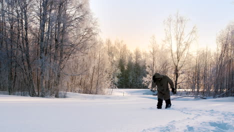 Static-view-of-a-man-in-a-heavy-coat-walking-through-deep-snow-in-frozen-park