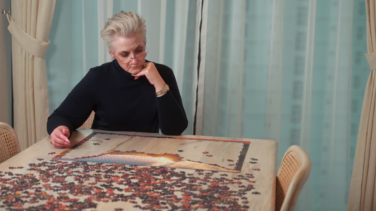 Elderly, lonely, divorced or widowed woman putting a large picture puzzle together